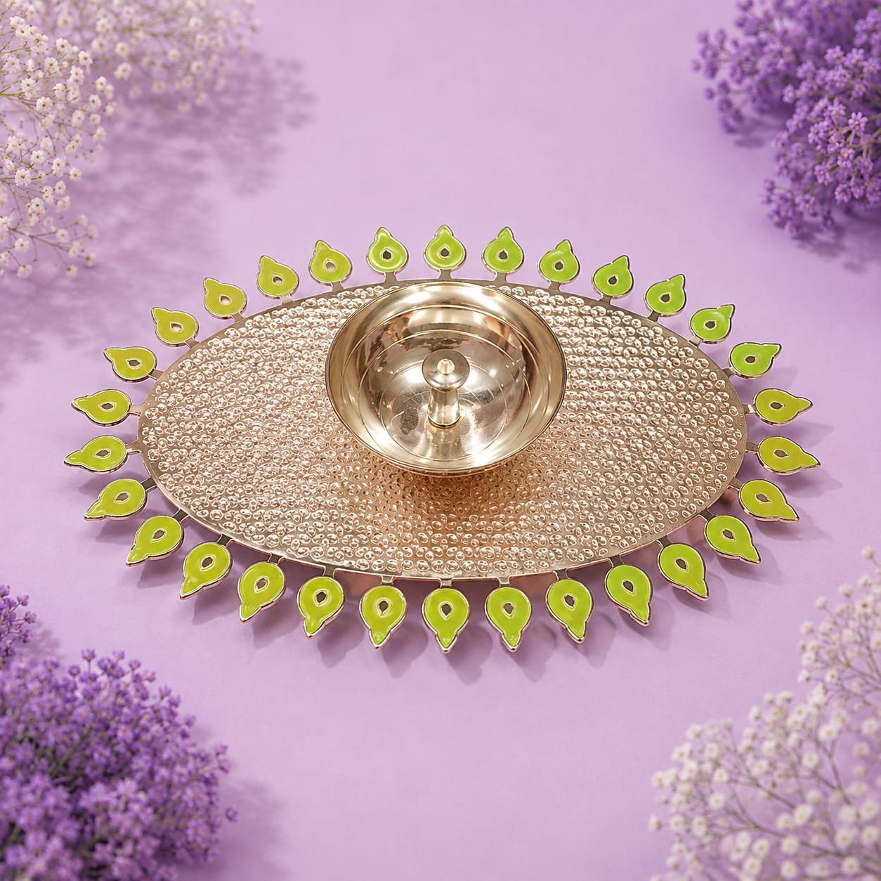 Gold-finish decorative metallic puja thali features an oval textured tray edged with vibrant lime-green leaf or diya-shaped motifs, centered with a matching small brass diya bowl.